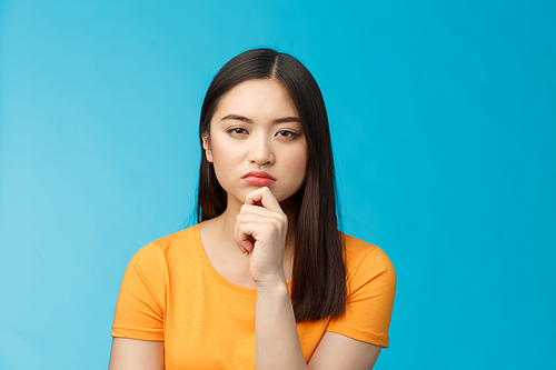 Close-up serious-looking suspicious female asian look disbelief, pondering, solving riddle, squinting hesitant disbelief, frowning suspect something wrong, thinking, focus stare, blue background.