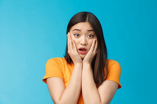 Close-up concerned shocked young timid asian girl gasping, dropping jaw feel sorry, pitty for friend open mouth stunned stare camera, grab face shook, speechless, frustrated, stand blue background.