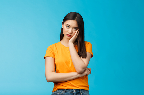 Sad bored asian female student attend boring uninteresting lecture lean face palm, look indifferent express apathy dislike, grimacing and sulking disappointed stand blue background bothered.