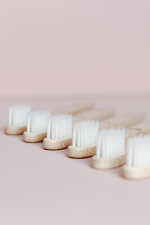 A super close up of some bamboo toothbrushes over a clear pink background