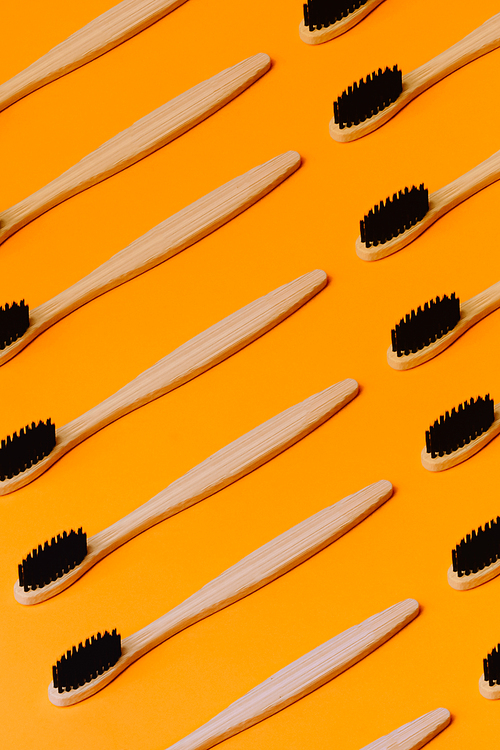 A minimalistic and repetitive patron of a lot of bamboo toothbrush over a orange background
