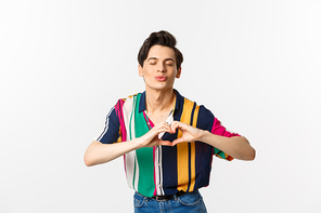 Lovely young man pucker lips and showing heart sign, waiting for kiss, I love you gesture, standing over white background.