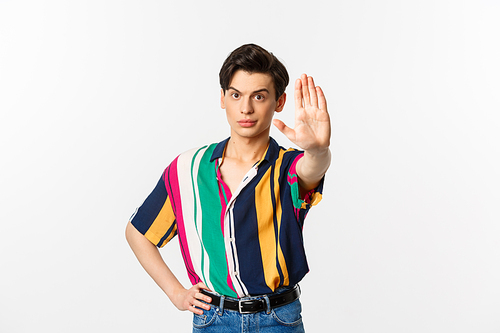 Young confident gay man saying no, showing stop sign and looking displeased, standing over white background.