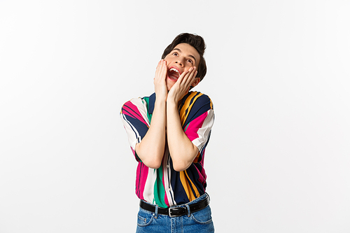 Image of excited gay man shouting of joy and looking up, feeling ecstatic, standing against white background.