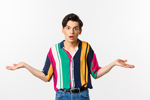 Confused young androgynous man spread hands and looking clueless, dont understand, standing puzzled against white background.
