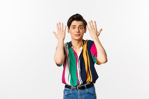Shocked and annoyed young man shaking hands and looking distressed, standing over white background.