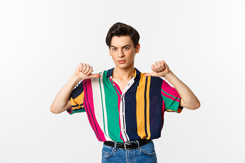 Confident and sassy gay man pointing at himself, looking self-assured, standing over white background.
