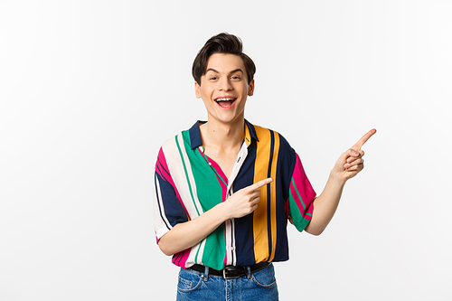 Happy gay man laughing and smiling, pointing fingers right at promo offer, standing over white background. Copy space
