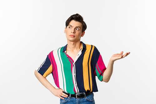 Confused gay man looking left at something strange, raising hand clueless and puzzled, standing over white background.