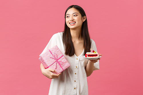 Celebration, party holidays and fun concept. Dreamy happy pretty birthday girl in white dress, smiling and looking away as receiving gift, eating b-day cake, pink background.