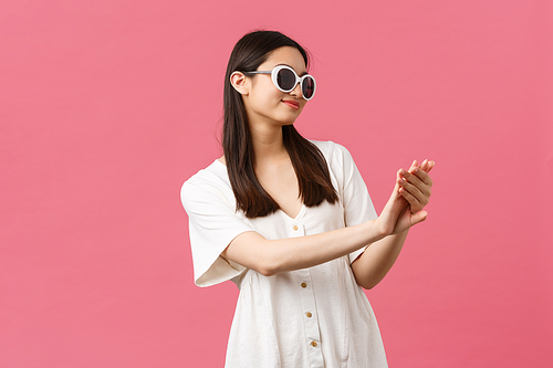 Beauty, people emotions and summer leisure and vacation concept. Smiling good-looking asian glamour girl looking at her manicure pleased after visiting nail studio, standing over pink background.