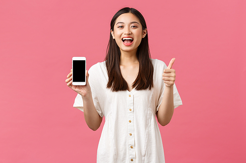 Beauty, people emotions and technology concept. Satisfied happy asian girl show thumbs-up as demonstrate mobile phone screen application, standing pink background recommend app.