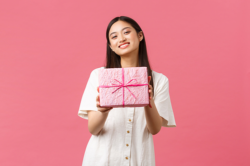 Celebration, party holidays and fun concept. Friendly beautiful asian girlfriend smiling, congratulating friend with birthday and giving gift, standing pink background. Copy space