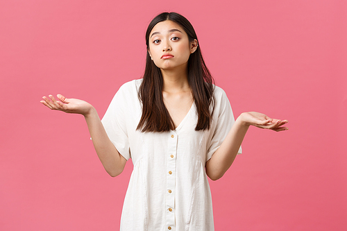 Beauty, people emotions and summer leisure concept. Clueless and careless cute asian girl in white dress, dont know anything, shrugging with reluctant face, standing pink background unaware.