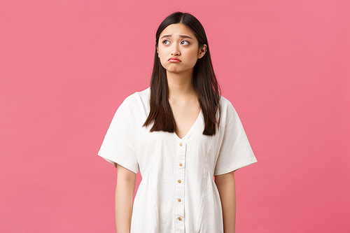 Beauty, people emotions and summer leisure concept. Sad and gloomy asian lonely girl looking upset and depressed, pouting and frowning as looking upper left corner, pink background.