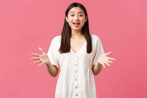 Beauty, people emotions and summer leisure concept. Excited happy cute asian girl describe amazing event, gesturing with hands and talking at camera joyful, stand pink background.