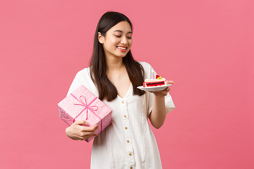 Celebration, party holidays and fun concept. Dreamy happy pretty birthday girl in white dress, smiling and looking away as receiving gift, eating b-day cake, pink background.