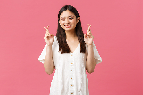 Beauty, people emotions and summer leisure concept. Optimistic asian girl having faith in dreams come true, cross fingers good luck and smiling happy camera, believe over pink background.