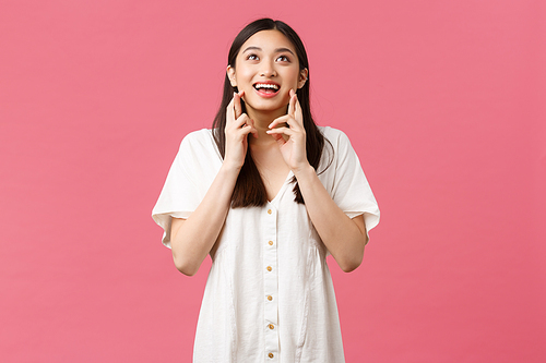 Beauty, people emotions and summer leisure concept. Dreamy asian girl in white dress making wish, looking hopeful sky as pleading god, cross fingers good luck, anticipating, pink background.