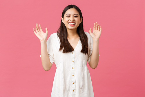 Beauty, people emotions and summer leisure concept. Happy smiling asian girl laughing and showing empty hands, raise arms and giggle, having fun over pink background.