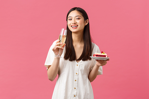 Celebration, party holidays and fun concept. Happy asian woman celebrating birthday enjoying tasty b-day cake and drinking champagne, smiling at camera joyful, pink background.