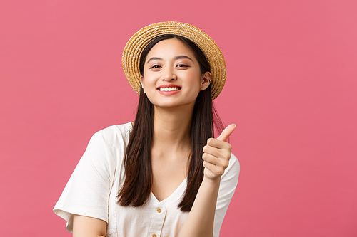 Beauty, people emotions and leisure and vacation concept. Close-up of satisfied cute asian female customer suggest awesome store with summer clothes, show thumbs-up, wear straw hat.