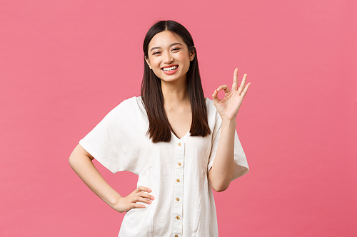 Beauty, people emotions and summer leisure and vacation concept. Confident cheerful asian girl having no problem, showing all good okay gesture and wink silly, encourage visit store, pink background.