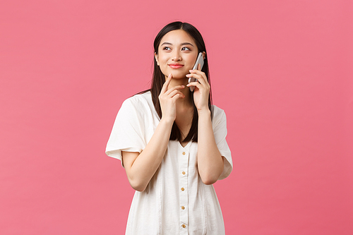 Beauty, people emotions and technology concept. Thoughtful asian girl making order delivery using smartphone, thinking while talking over phone, looking up, pondering as choosing, pink background.