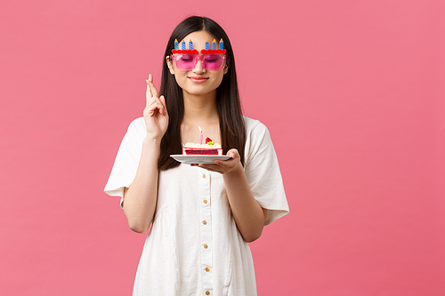 Celebration, party holidays and fun concept. Smiling happy birthday girl making wish on b-day cake, close eyes and cross fingers good luck, want dream come true, pink background.