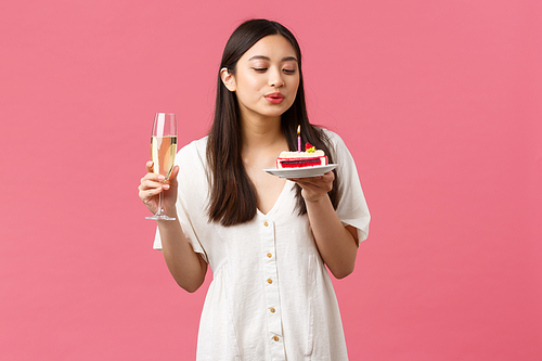 Celebration, party holidays and fun concept. Glamour elegant good-looking asian woman celebrating her birthday, holding glass champagne making wish as blowing lit candle on b-day cake.