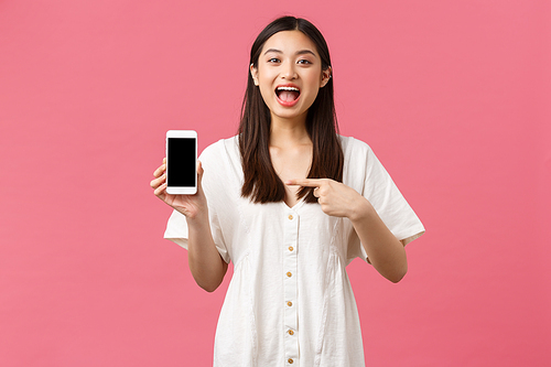 Beauty, people emotions and technology concept. Excited pretty young woman make announcement, pointing finger at mobile phone display and smiling thrilled, showing awesome app.