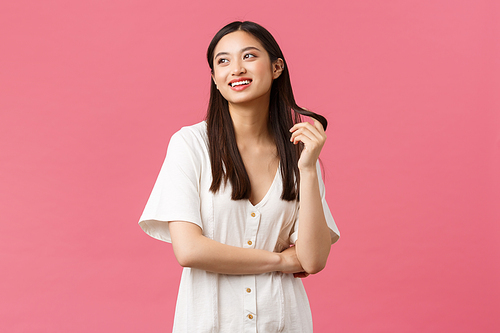 Beauty, people emotions and summer leisure concept. Dreamy asian girl in white dress, imaging something with silly smile, playing with hair strand and looking top left corner, white background.