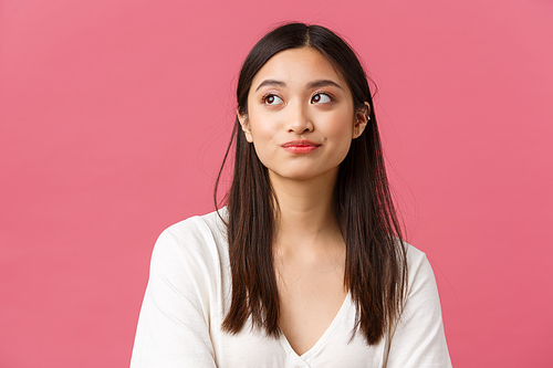 Beauty salon, haircare and skincare products advertisement concept. Thoughtful attractive asian female lifestyle blogger looking away, thinking hesitant, standing pink background.