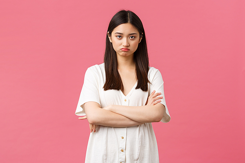 Beauty, people emotions and summer leisure concept. Gloomy insulted timid asian girl feeling offended and displeased, cross arms on chest, pouting upset, complaining, pink background.