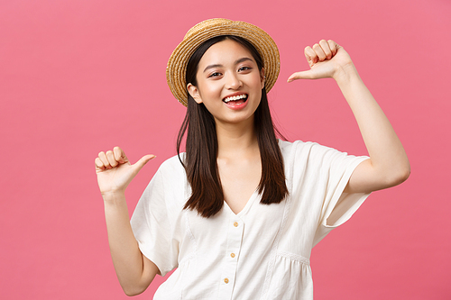 Beauty, people emotions and summer leisure and vacation concept. Close-up of happy enthusiastic female asian tourist in straw hat pointing at herself and smiling, bragging over pink background.