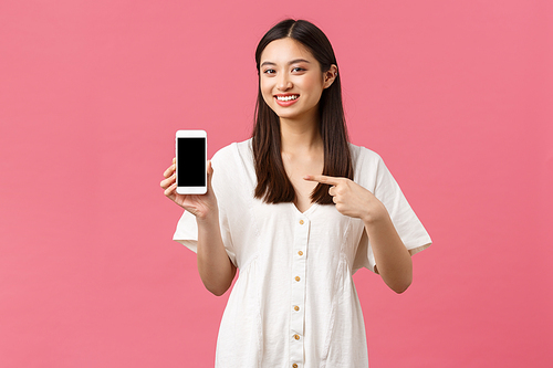 Beauty, people emotions and technology concept. Pretty stylish korean girl showing application on smartphone screen. Woman promoting store or app, pointing finger at mobile phone and smiling.