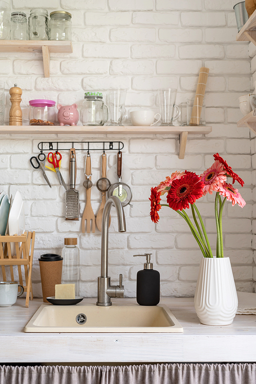 Rustic kitchen interior with white brick wall and white wooden shelves. Fresh gerbera flowers in a white vase