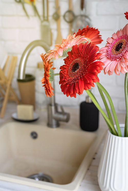 Rustic kitchen interior with white brick wall and white wooden shelves. Fresh gerbera flowers in a white vase