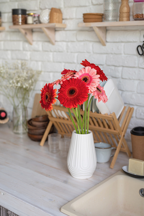 Rustic kitchen interior with white brick wall and white wooden shelves. Fresh gerbera flowers in a white vase