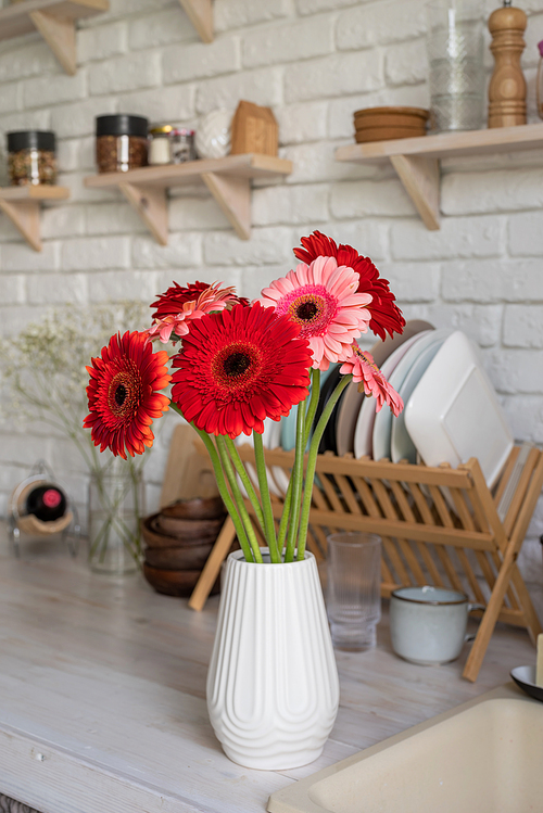 Rustic kitchen interior with white brick wall and white wooden shelves. Fresh gerbera flowers in a white vase