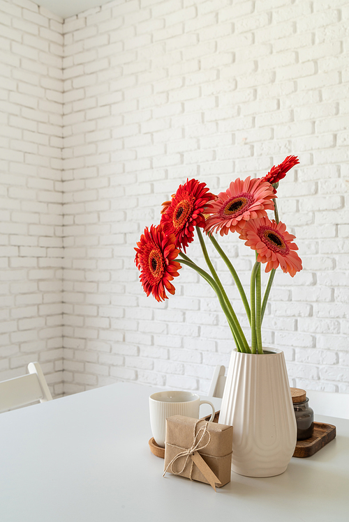 Happy birthday gerbera daisy flowers in a vase with a craft gift box on white kitchen table, minimal style