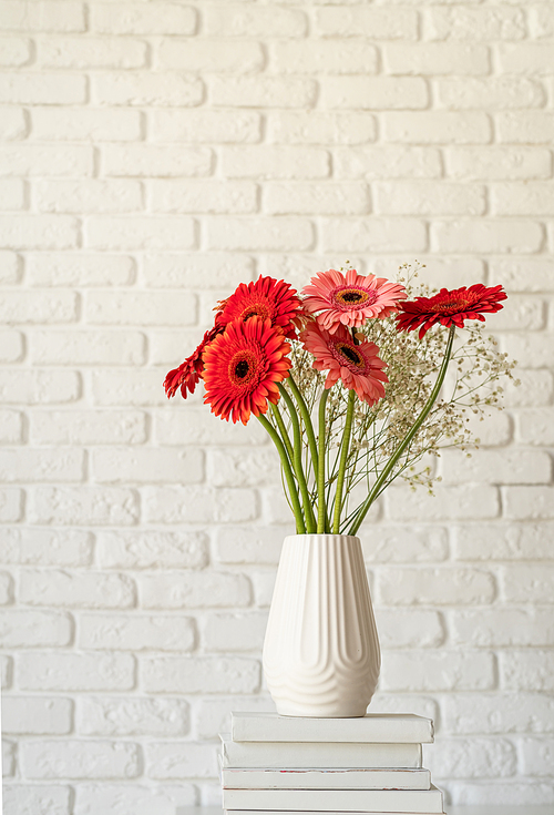 Red and pink gerbera daisies in white vase on stack of books, minimal style, mock up design