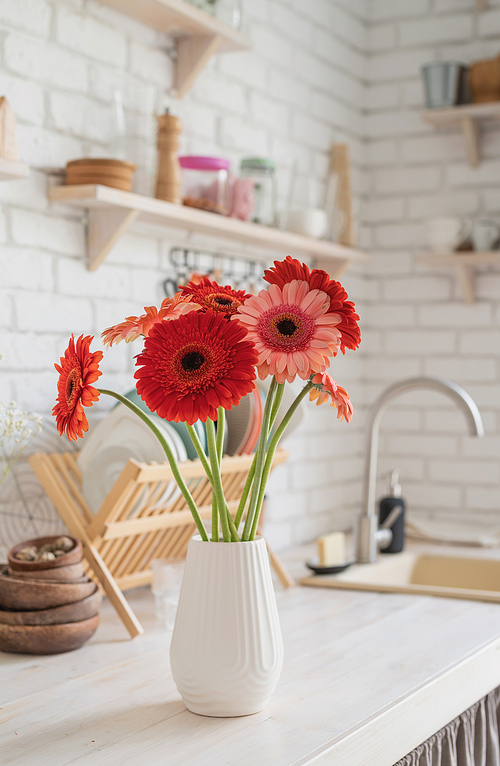 Rustic kitchen interior with white brick wall and white wooden shelves. Fresh gerbera flowers in a white vase