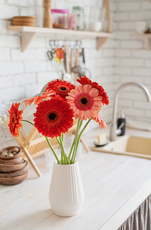 Rustic kitchen interior with white brick wall and white wooden shelves. Fresh gerbera flowers in a white vase