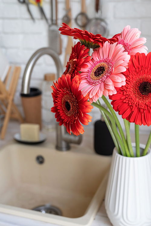 Rustic kitchen interior with white brick wall and white wooden shelves. Fresh gerbera flowers in a white vase