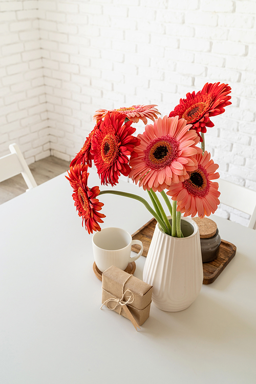 Happy birthday gerbera daisy flowers in a vase with a craft gift box on white kitchen table, minimal style