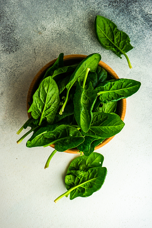 Wooden bowl full of organic fresh baby spinach leaves on white concrete background