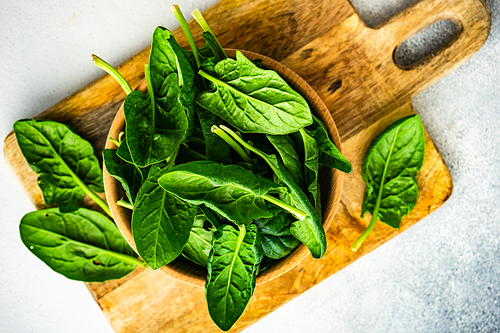 Wooden bowl full of organic fresh baby spinach leaves on white concrete background