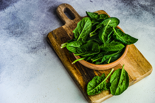Wooden bowl full of organic fresh baby spinach leaves on white concrete background