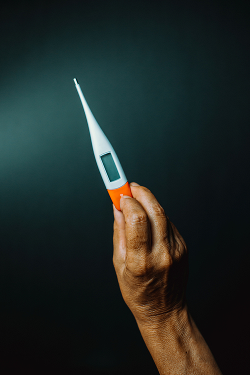 Old hand grabbing a thermometer over a dark background